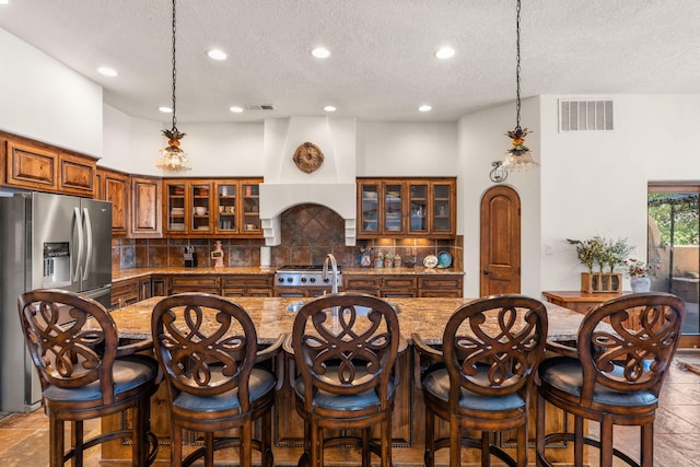 746 Chamisal Rd NW, Los Ranchos, NM 87107 - kitchen with stainless steel refrigerator with ice dispenser, brown cabinetry, a textured ceiling, backsplash, and a kitchen breakfast bar