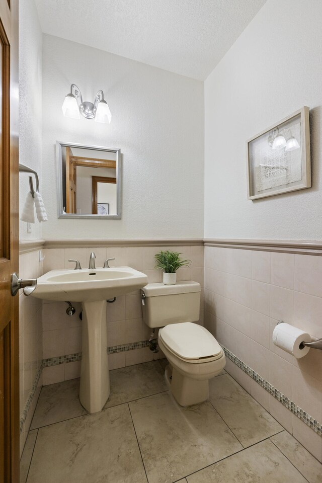 8712 Greenarbor Rd NE, Albuquerque, NM 87122 - half bath with tile walls, a textured ceiling, and a wainscoted wall