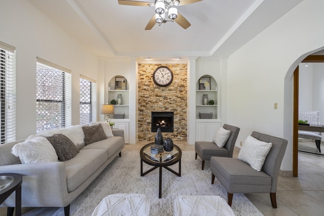 8712 Greenarbor Rd NE, Albuquerque, NM 87122 - living room featuring built in shelves, ceiling fan, arched walkways, light tile patterned flooring, and a raised ceiling