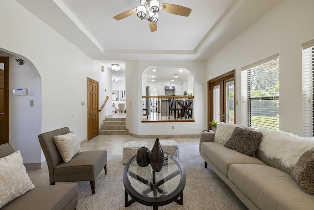 8712 Greenarbor Rd NE, Albuquerque, NM 87122 - living room featuring arched walkways, a ceiling fan, stairs, a tray ceiling, and light tile patterned flooring