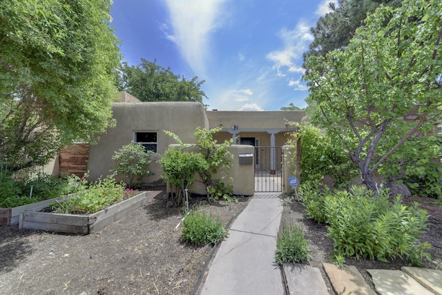 1228 Lafayette Dr NE, Albuquerque, NM 87106 - pueblo-style house with a gate, a fenced front yard, stucco siding, and a vegetable garden