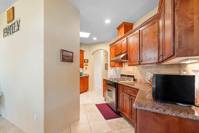 3 Seasons Cir, Placitas, NM 87043 - kitchen featuring stainless steel gas range oven, under cabinet range hood, backsplash, arched walkways, and dark stone countertops