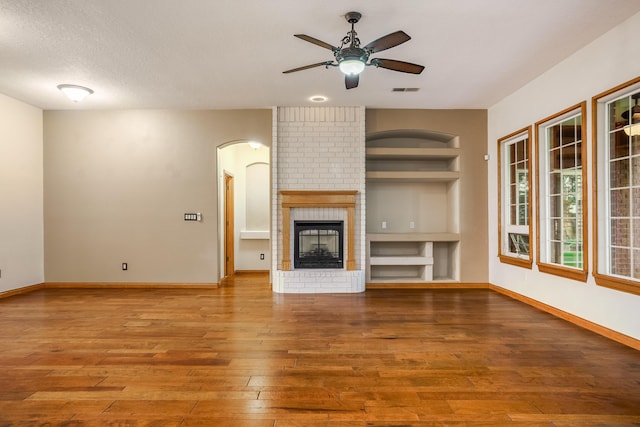 924 Seattle Slew Ave SE, Albuquerque, NM 87112 - unfurnished living room featuring built in shelves, wood-type flooring, a ceiling fan, arched walkways, and a brick fireplace