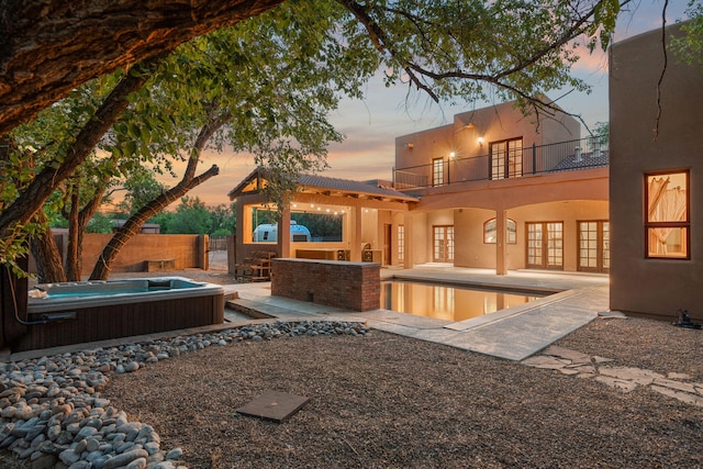 9005 4th St NW, Albuquerque, NM 87114 - back of property at dusk with french doors, an outdoor hot tub, a patio, stucco siding, and a fenced backyard