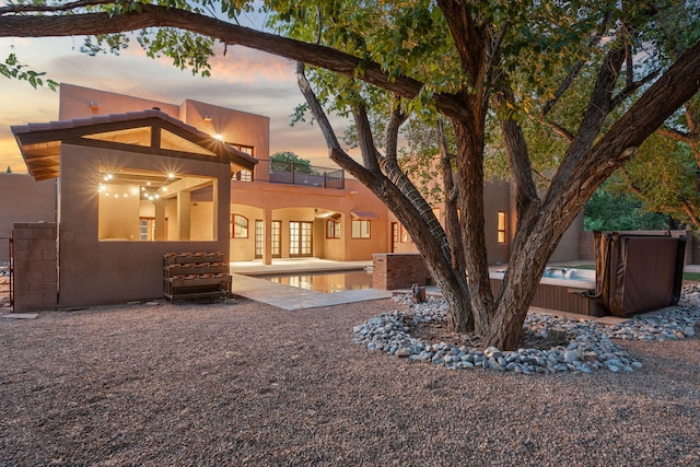 9005 4th St NW, Albuquerque, NM 87114 - back of property at dusk with a balcony, a hot tub, stucco siding, a patio, and an outdoor pool