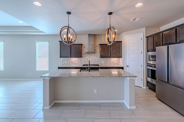 4289 Crowned Eagle Loop NE, Rio Rancho, NM 87144 - kitchen with appliances with stainless steel finishes, wall chimney exhaust hood, decorative backsplash, dark brown cabinetry, and a chandelier