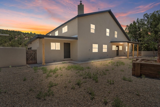 7 Corte De Canoncito, Cedar Crest, NM 87008 - back of house at dusk with a gate, stucco siding, a chimney, and a patio