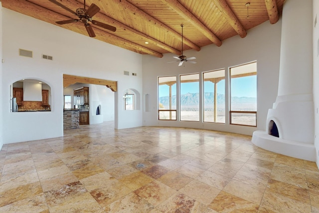 3 Quiet Ln, Corrales, NM 87048 - unfurnished living room featuring a wooden ceiling with exposed beams, a ceiling fan, stone tile flooring, a high ceiling, and arched walkways