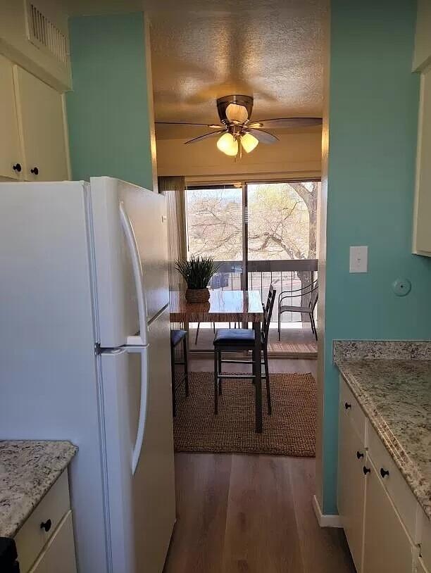 4601 Carlisle Blvd NE Unit H-2, Albuquerque, NM 87109 - kitchen with freestanding refrigerator, white cabinets, a ceiling fan, dark wood finished floors, and light stone counters