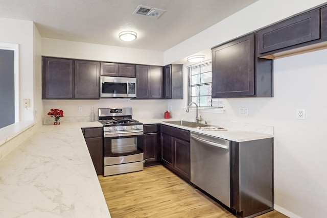 4807 Parsifal St NE, Albuquerque, NM 87111 - kitchen featuring stainless steel appliances, dark brown cabinetry, light wood-style flooring, and light stone counters