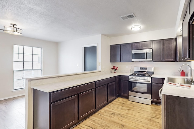 4807 Parsifal St NE, Albuquerque, NM 87111 - kitchen featuring appliances with stainless steel finishes, dark brown cabinetry, a textured ceiling, light wood-style flooring, and a peninsula