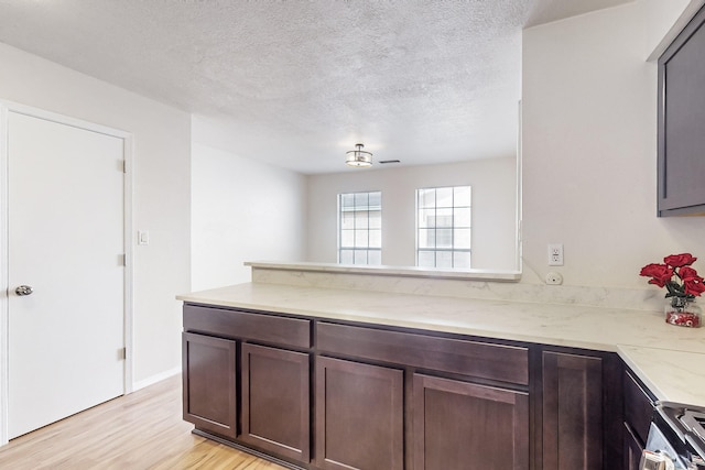 4807 Parsifal St NE, Albuquerque, NM 87111 - kitchen with light wood-style floors, a peninsula, a textured ceiling, dark brown cabinets, and light stone counters