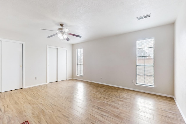 4807 Parsifal St NE, Albuquerque, NM 87111 - unfurnished bedroom featuring multiple windows, multiple closets, light wood-style floors, a textured ceiling, and a ceiling fan