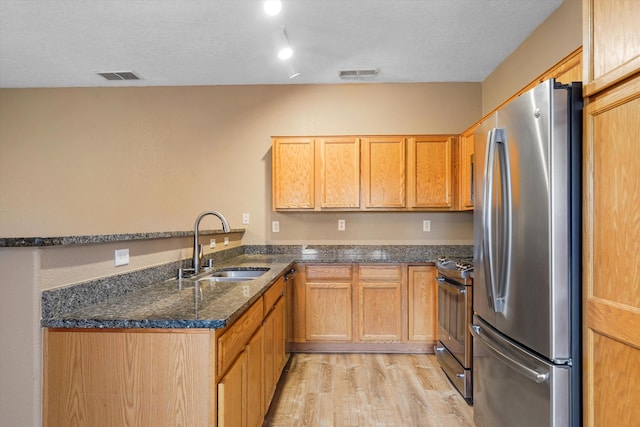 5443 Reserve Ct NE, Rio Rancho, NM 87144 - kitchen with appliances with stainless steel finishes, a peninsula, light wood-type flooring, dark stone counters, and a textured ceiling