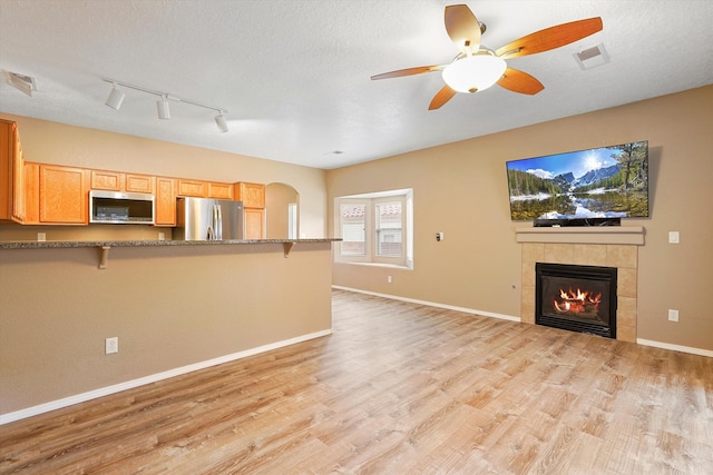 5443 Reserve Ct NE, Rio Rancho, NM 87144 - kitchen with stainless steel appliances, a breakfast bar area, light wood finished floors, a fireplace, and a textured ceiling