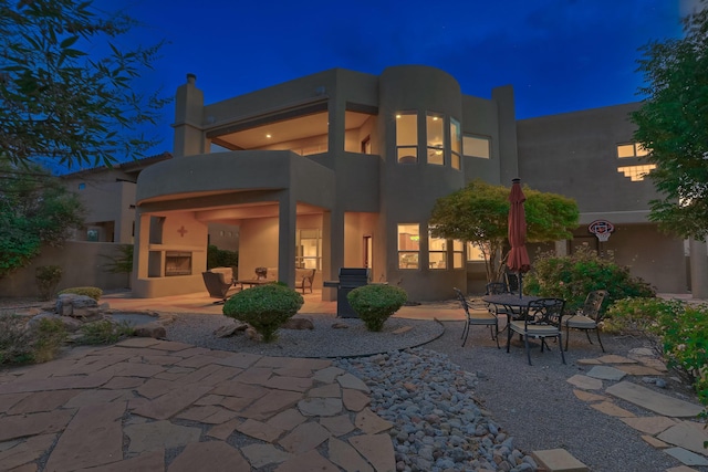 9404 Bear Mountain Trl NE, Albuquerque, NM 87113 - back of house at twilight with a patio area, stucco siding, a large fireplace, and a balcony