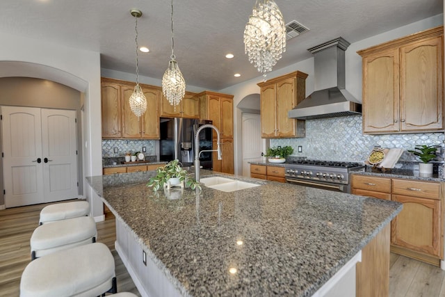 42 Los Pecos Loop, Tijeras, NM 87059 - kitchen with wall chimney exhaust hood, high end stainless steel range oven, fridge with ice dispenser, arched walkways, and an island with sink