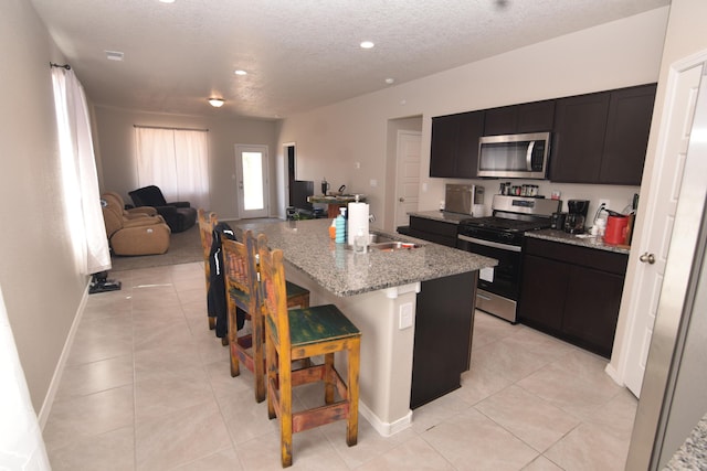 10812 Caresso SW, Albuquerque, NM 87121 - kitchen featuring stainless steel appliances, open floor plan, a textured ceiling, a kitchen bar, and an island with sink