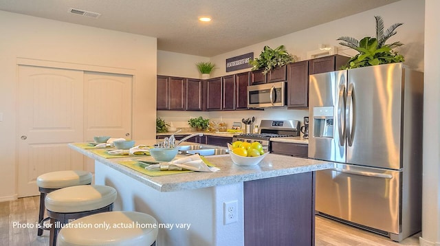 1652 Maggie Ct NE, Rio Rancho, NM 87144 - kitchen featuring stainless steel appliances, light wood-type flooring, dark brown cabinetry, a breakfast bar, and light countertops