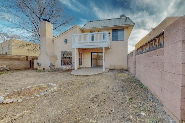 9815 Osuna Rd NE, Albuquerque, NM 87111 - back of house featuring a balcony, stucco siding, a fenced backyard, a chimney, and a metal roof