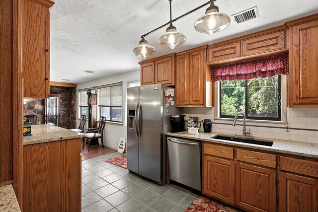 411 Schmidt Pl, Los Lunas, NM 87031 - kitchen featuring appliances with stainless steel finishes, healthy amount of natural light, brown cabinetry, a textured ceiling, and tasteful backsplash