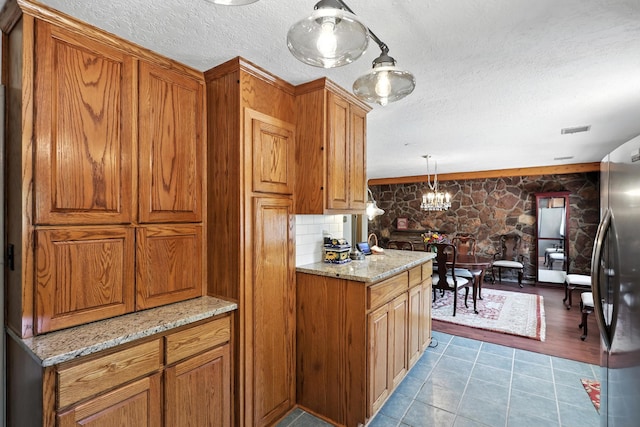 411 Schmidt Pl, Los Lunas, NM 87031 - kitchen featuring brown cabinetry, a textured ceiling, a chandelier, freestanding refrigerator, and light stone countertops