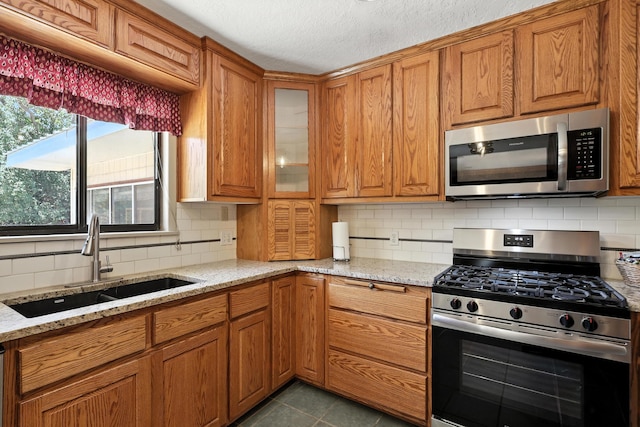 411 Schmidt Pl, Los Lunas, NM 87031 - kitchen featuring appliances with stainless steel finishes, brown cabinetry, tasteful backsplash, light stone countertops, and glass insert cabinets