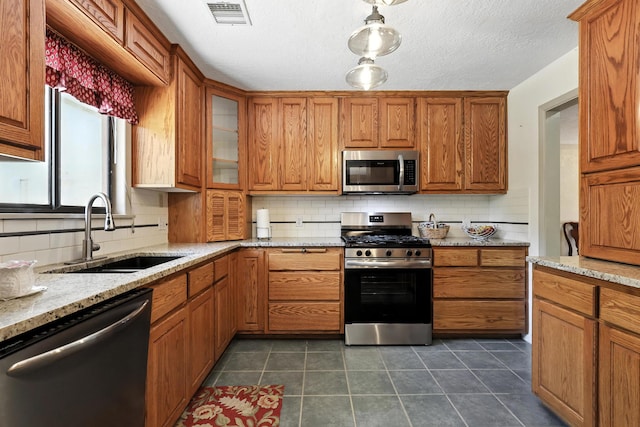 411 Schmidt Pl, Los Lunas, NM 87031 - kitchen featuring appliances with stainless steel finishes, brown cabinets, tasteful backsplash, and light stone counters