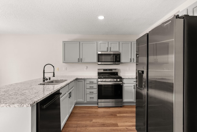 716 Palo Duro Dr, Bernalillo, NM 87004 - kitchen with appliances with stainless steel finishes, a peninsula, a textured ceiling, light wood-type flooring, and light stone countertops