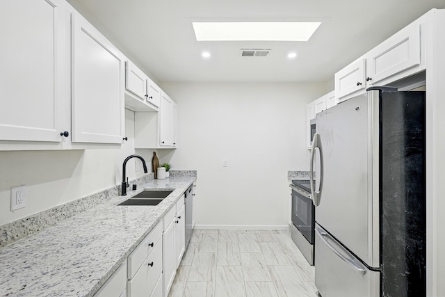 1202 Truman St SE, Albuquerque, NM 87108 - kitchen with appliances with stainless steel finishes, a skylight, white cabinetry, light stone countertops, and light marble finish floors