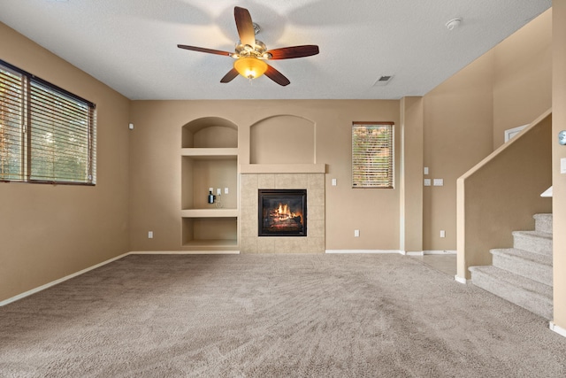 1717 Cortina Loop SE, Rio Rancho, NM 87124 - unfurnished living room featuring built in features, ceiling fan, a tiled fireplace, carpet flooring, and a textured ceiling