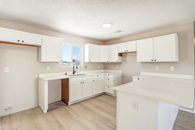1004 11th St SE, Rio Rancho, NM 87124 - kitchen with light wood-style floors, white cabinetry, a peninsula, light countertops, and a textured ceiling