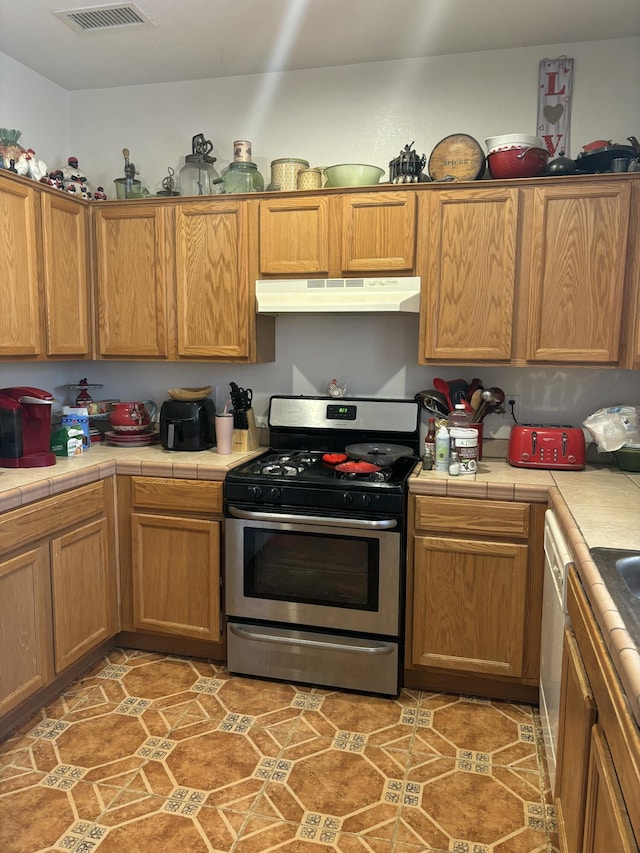 9523 Akutan Ct NW, Albuquerque, NM 87120 - kitchen with gas stove, tile counters, under cabinet range hood, and brown cabinets