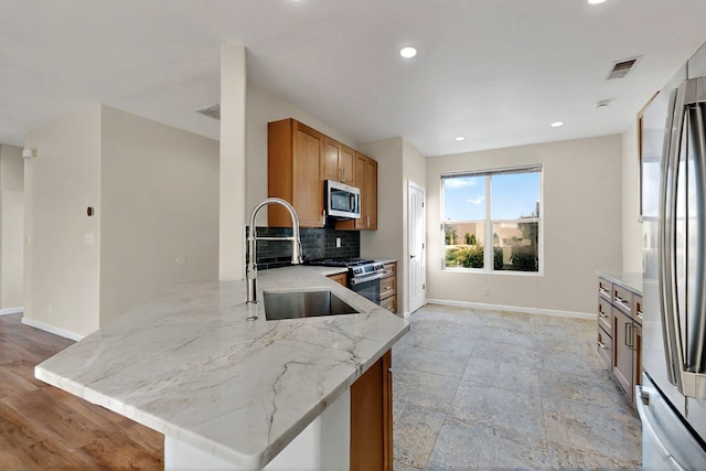5 Woodflower Pl, Santa Fe, NM 87508 - kitchen featuring appliances with stainless steel finishes, light stone counters, tasteful backsplash, brown cabinetry, and a peninsula