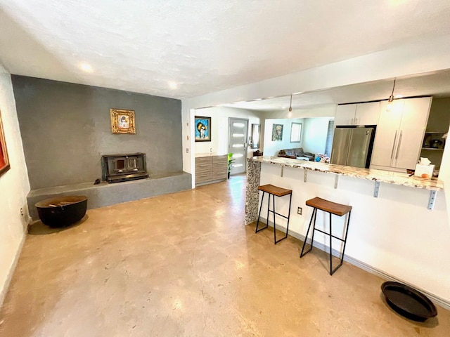 201 Marlowe Ln, Albuquerque, NM 87113 - kitchen featuring freestanding refrigerator, concrete flooring, a breakfast bar, white cabinetry, and a wood stove