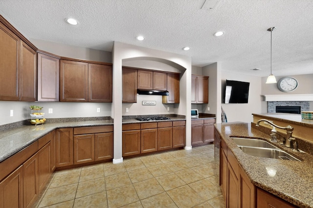 4420 Bentgrass Mdws NE, Rio Rancho, NM 87144 - kitchen with gas cooktop, under cabinet range hood, a textured ceiling, dark stone countertops, and brown cabinetry