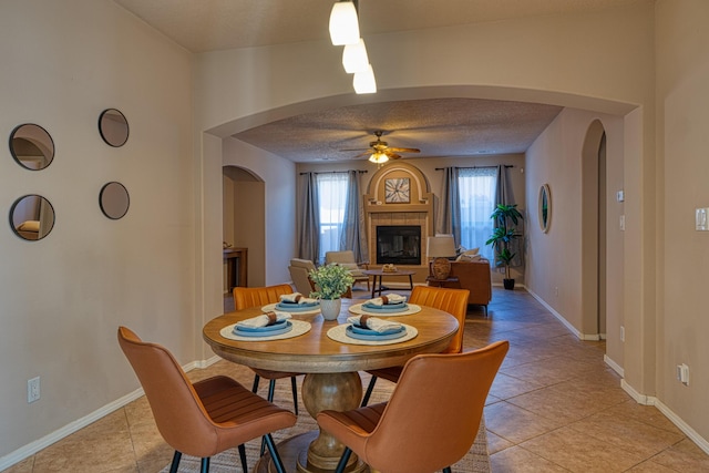 851 Vista Patron Dr, Bernalillo, NM 87004 - dining room featuring arched walkways, a ceiling fan, a tiled fireplace, and light tile patterned floors