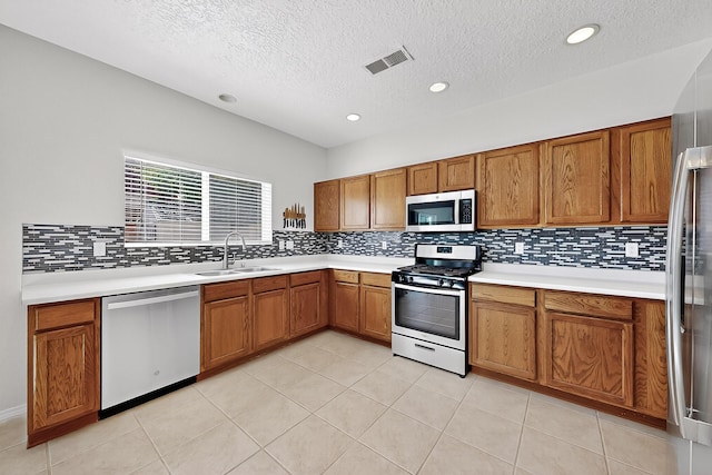 8905 Balsam Glade Rd NW, Albuquerque, NM 87114 - kitchen featuring stainless steel appliances, brown cabinets, a textured ceiling, backsplash, and light countertops