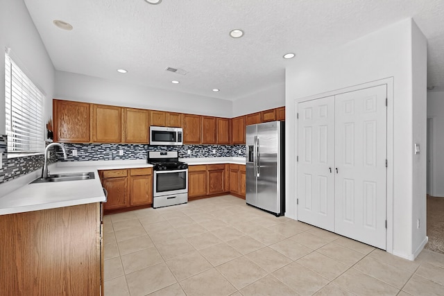 8905 Balsam Glade Rd NW, Albuquerque, NM 87114 - kitchen featuring appliances with stainless steel finishes, brown cabinets, tasteful backsplash, a textured ceiling, and light tile patterned floors