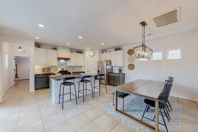 5716 Strand Loop SE, Albuquerque, NM 87106 - kitchen with appliances with stainless steel finishes, a breakfast bar, dark countertops, light tile patterned floors, and a kitchen island with sink