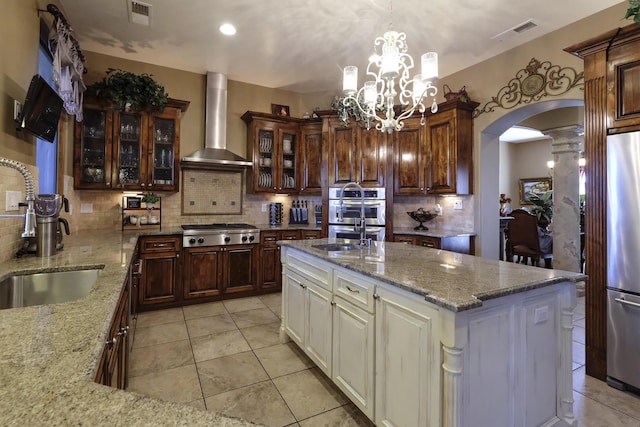 9604 Big Sage Dr NW, Albuquerque, NM 87114 - kitchen featuring wall chimney exhaust hood, appliances with stainless steel finishes, arched walkways, and backsplash