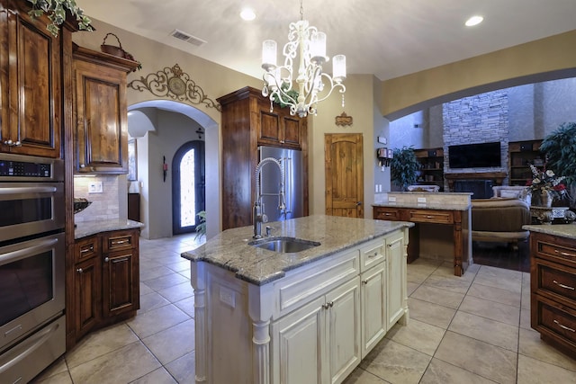 9604 Big Sage Dr NW, Albuquerque, NM 87114 - kitchen featuring stainless steel appliances, a warming drawer, arched walkways, a center island with sink, and light tile patterned floors
