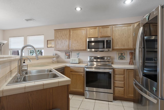 10027 Vista Cantera Ln NW, Albuquerque, NM 87114 - kitchen featuring appliances with stainless steel finishes, tile countertops, light tile patterned flooring, a peninsula, and a textured ceiling