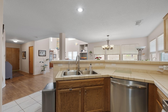 10027 Vista Cantera Ln NW, Albuquerque, NM 87114 - kitchen featuring stainless steel dishwasher, a textured ceiling, a chandelier, brown cabinets, and light tile patterned flooring