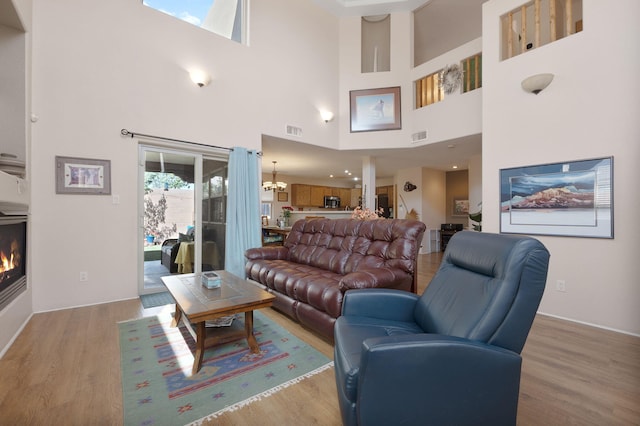 10027 Vista Cantera Ln NW, Albuquerque, NM 87114 - living area with light wood-style floors, a warm lit fireplace, a high ceiling, and a chandelier