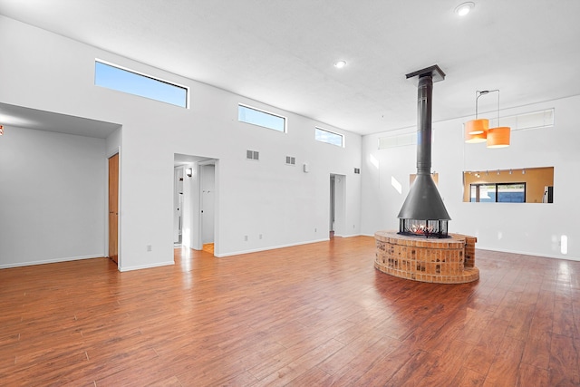 504 Ortiz Dr NE, Albuquerque, NM 87108 - unfurnished living room featuring a wood stove, wood finished floors, recessed lighting, a high ceiling, and plenty of natural light