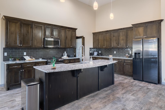 24 Norte Trl, Placitas, NM 87043 - kitchen featuring stainless steel appliances, decorative backsplash, dark brown cabinets, an island with sink, and a towering ceiling