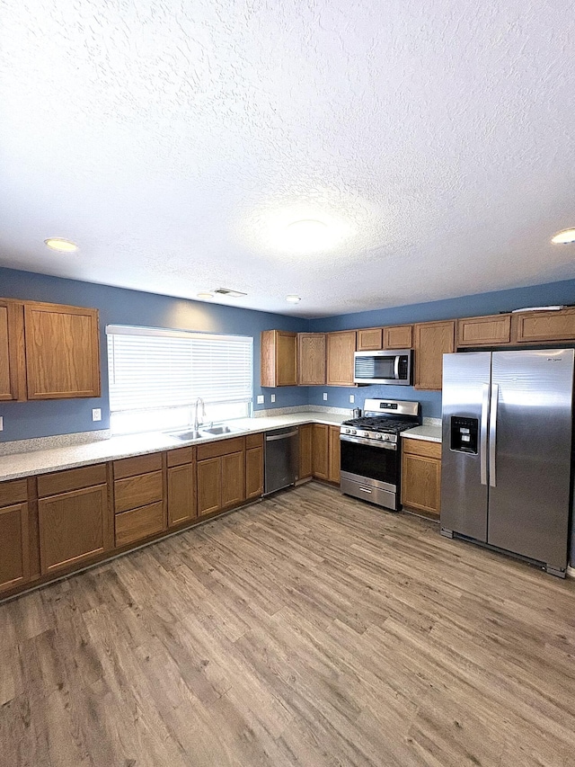 1543 White Pine Dr, Rio Rancho, NM 87144 - kitchen featuring appliances with stainless steel finishes, a textured ceiling, brown cabinetry, and wood finished floors
