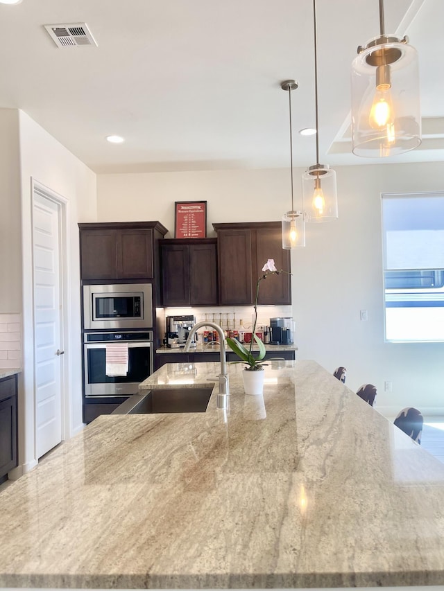 3237 Fennel Rd NE, Rio Rancho, NM 87144 - kitchen with stainless steel appliances, a large island, light stone counters, dark brown cabinetry, and backsplash
