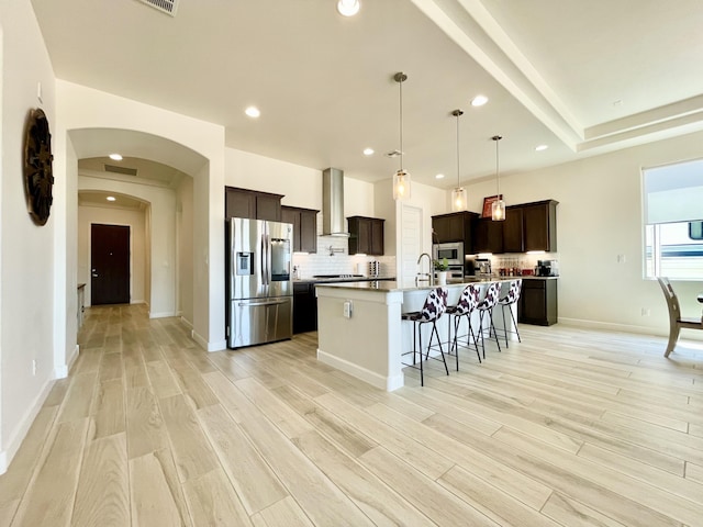 3237 Fennel Rd NE, Rio Rancho, NM 87144 - kitchen with appliances with stainless steel finishes, wall chimney range hood, a kitchen bar, tasteful backsplash, and dark brown cabinetry